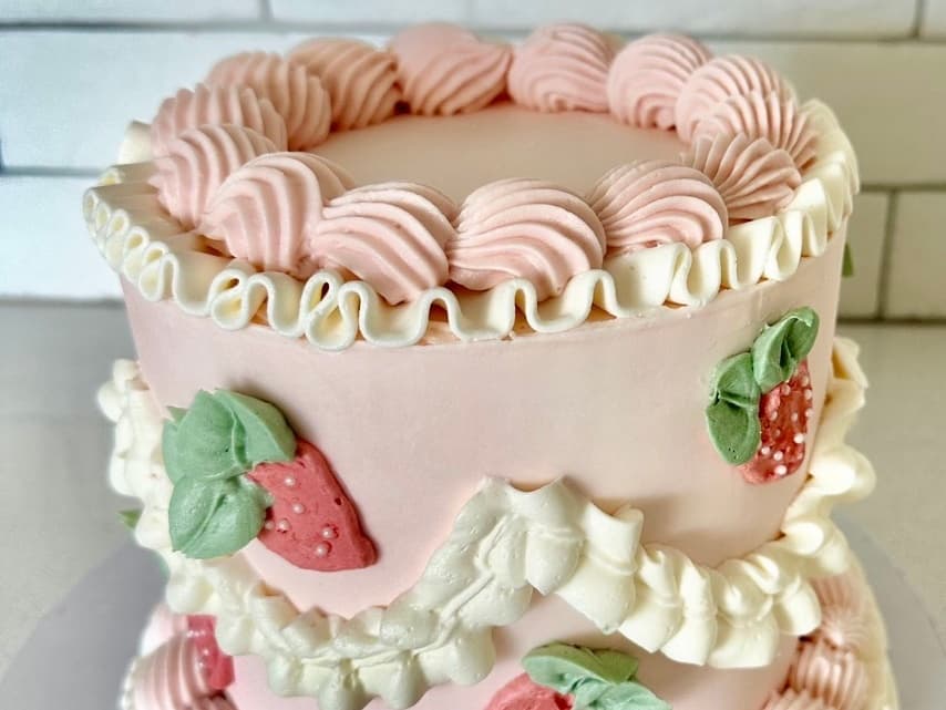 Pink two-tiered smash cake with white ruffle piping and strawberry decorations