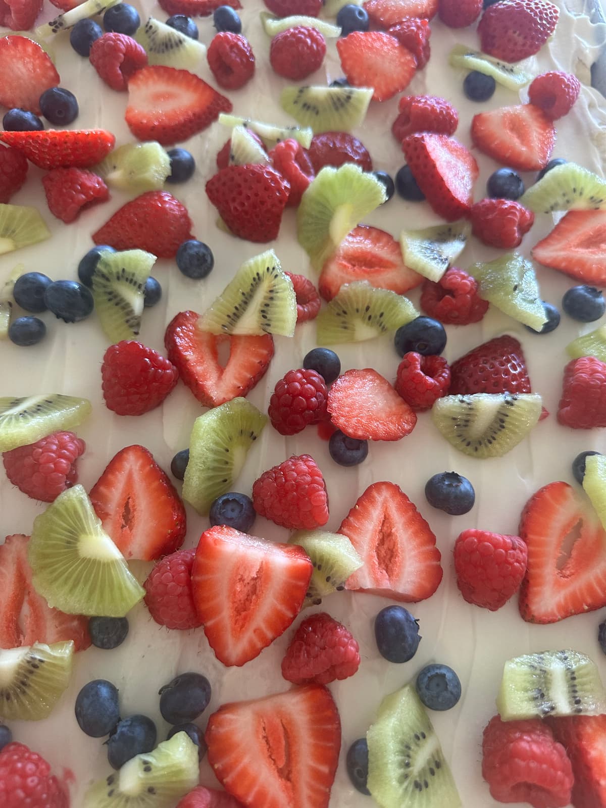Fruit pizza bars topped with sweet cream cheese frosting, strawberries, kiwi, raspberries, and blueberries