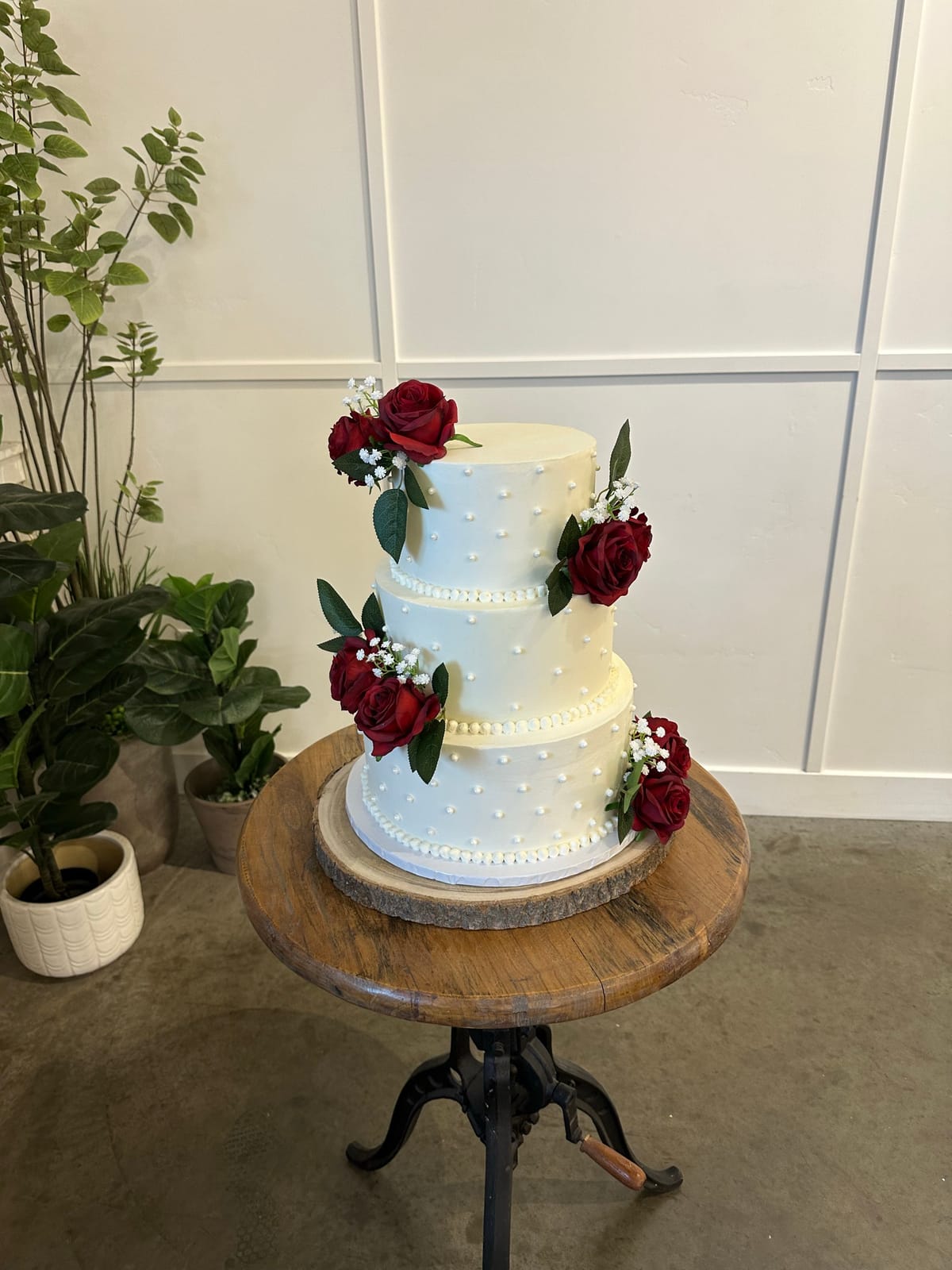 Three-tier white wedding cake with red roses and baby's breath on a rustic wooden stand